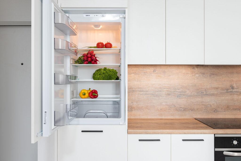 Contemporary kitchen with refrigerator filled with fresh bright tomatoes lettuce and bell peppers,