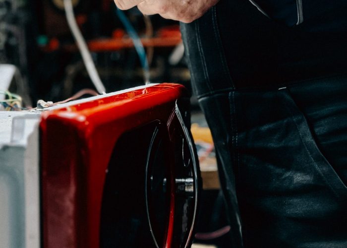 Electrician working on red microwave repair in a workshop setting, tools in hand, Winston-Salem appliance repair