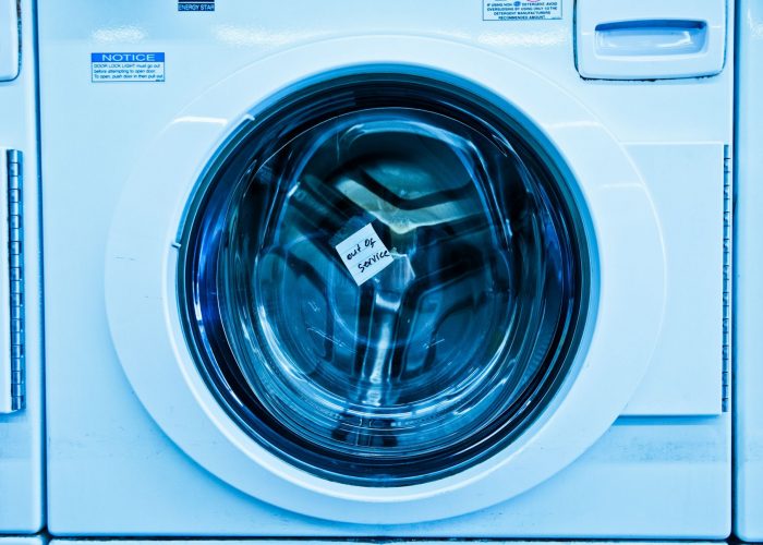 Close-up of an out-of-service washing machine in a laundromat with a blue tint.